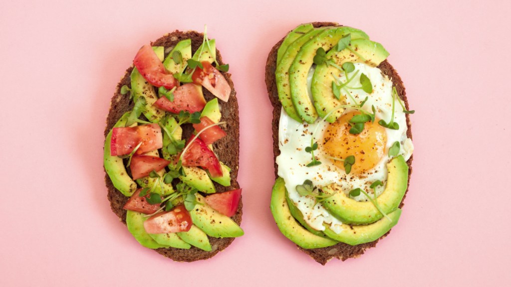 Avocado toast, a potassium-rich food, on a pink background and topped with diced tomatoes and egg