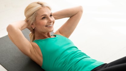 A blonde woman in a green tank top lying on the floor with her hands behind her head doing one of the best ab workouts for women