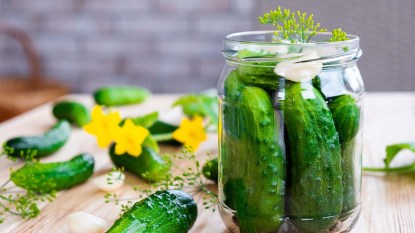 Glass jar with fresh cucumbers, herbs, garlic, and dill on wooden board