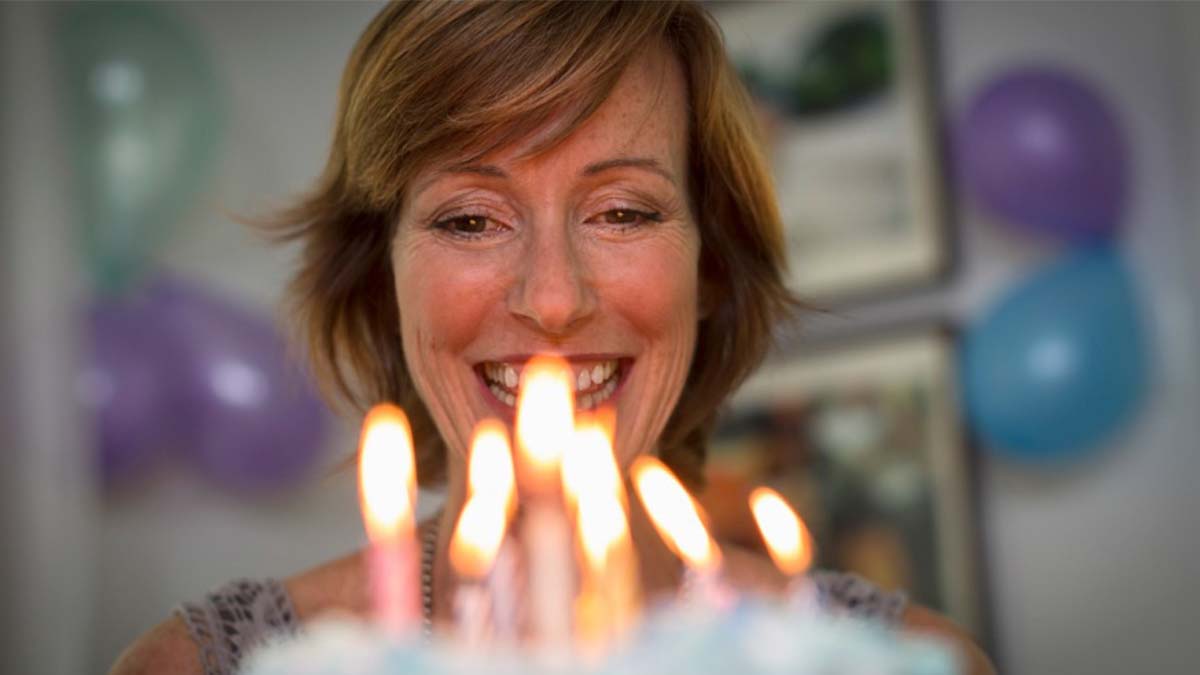 Женщина собирается задуть свечи на праздничном торте