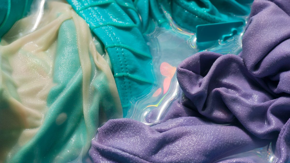 blue and purple swimsuits being washed by hand with water and dish soap
