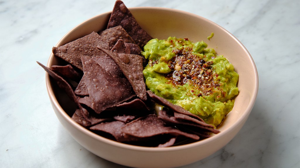 Bowl of blue corn tortilla chips with a dollop of guacamole topped with chia seeds