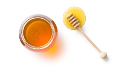 honey in a jar with a honey dipper on white surface