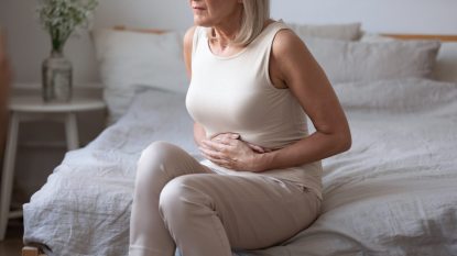 mature woman feeling hungry, sitting on a bed holding her stomach