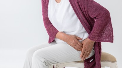 mature woman wearing a cardigan holding her hip, hip pain
