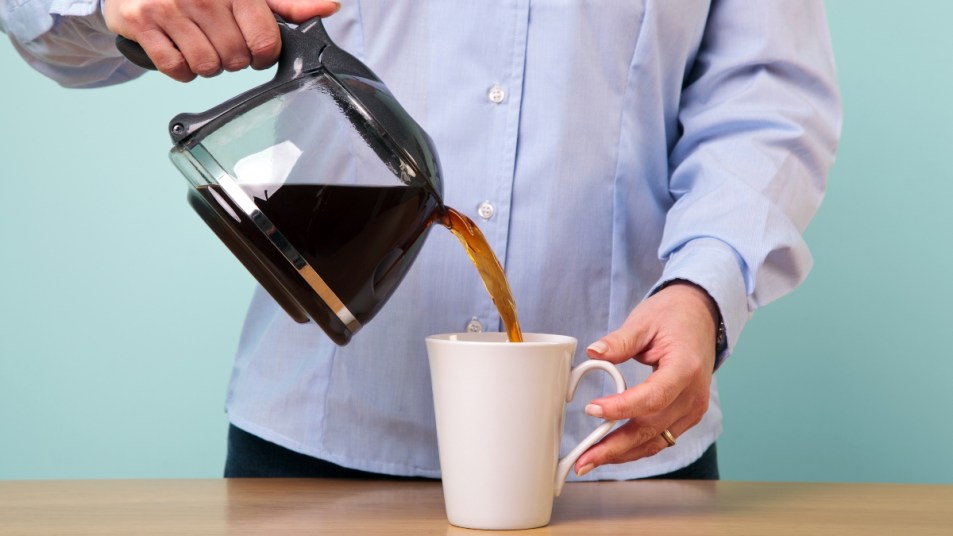 Photo of a woman on her break pouring herself a mug of hot filtered coffee from a glass pot.