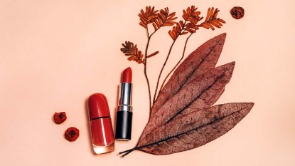 Decorative flat lay composition with cosmetics, woman beauty products, red lipstick, nail polish, decorated with autumn leaves and berries