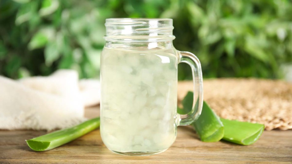 Fresh aloe drink in mason jar and leaves on wooden table