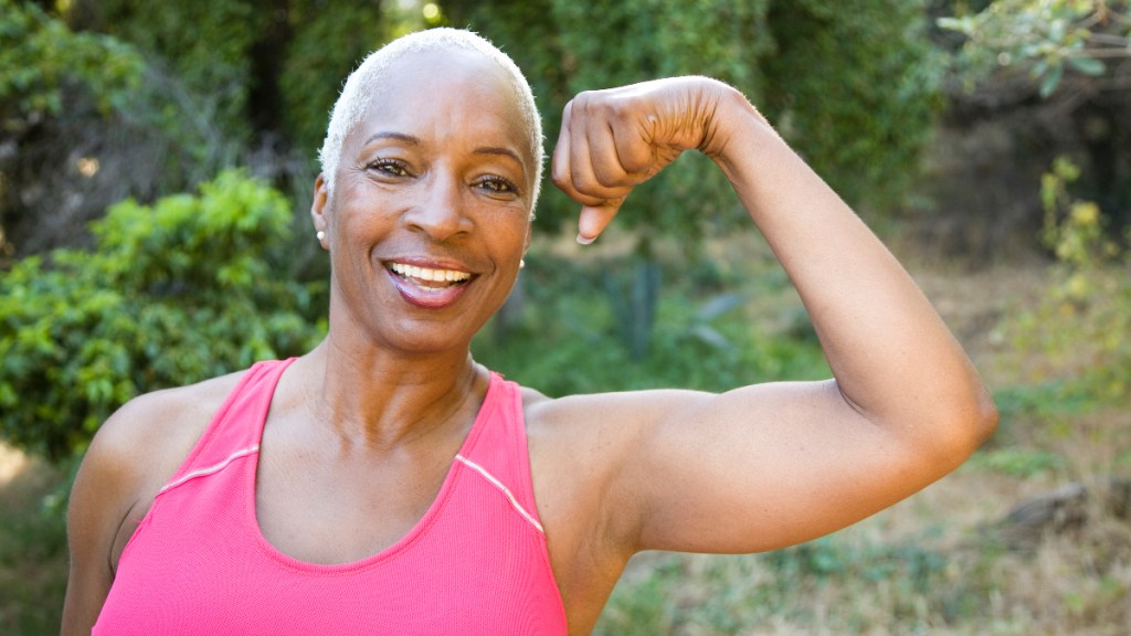 A woman with short hair wearing a pink tank top flexing her arm