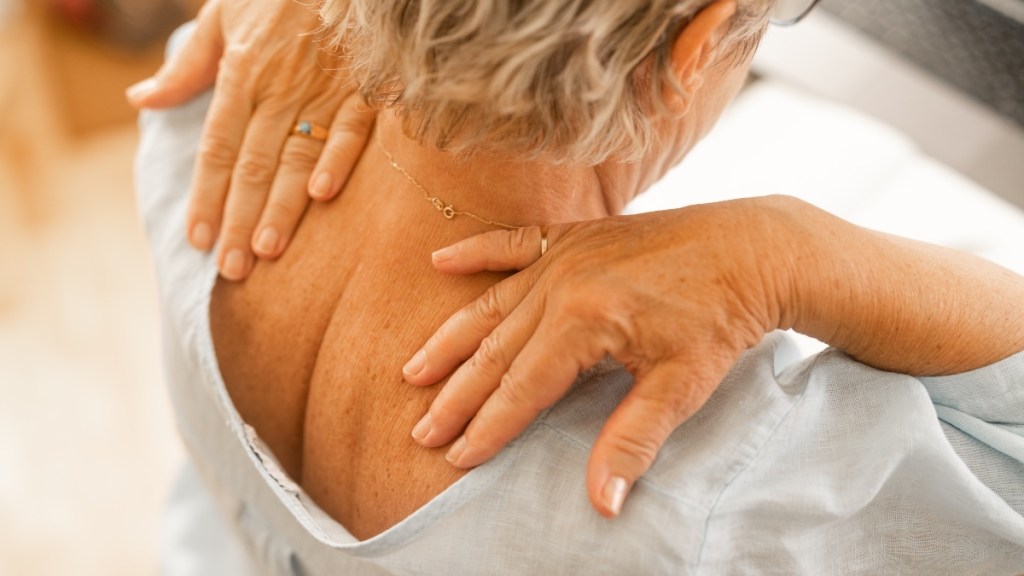 An older woman with her hands on the back of her neck, which has a hump