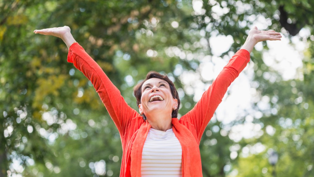 A woman in a bright top raising her arms in the air happy and energized
