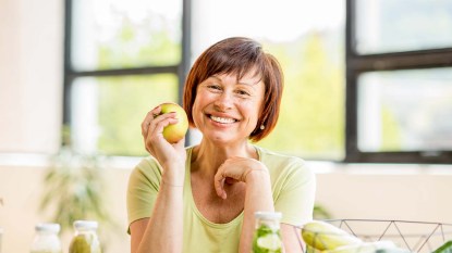 Portrait of a beautiful older woman with green healthy food on the table indoors