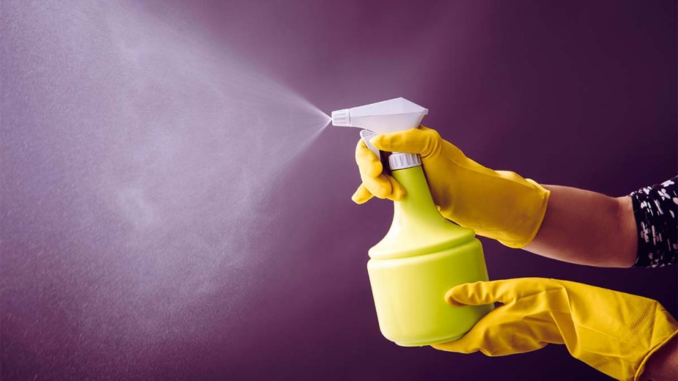 Woman wearing yellow rubber gloves using green spray bottle and spraying liquid mist in air