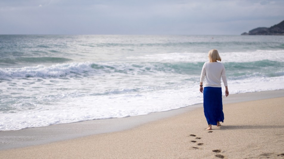 mature woman in blue skirt walking down to the water on a beach, for mental health