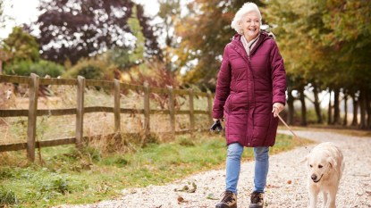 mature woman in red coat walking her dog in the fall as a way to improve vision