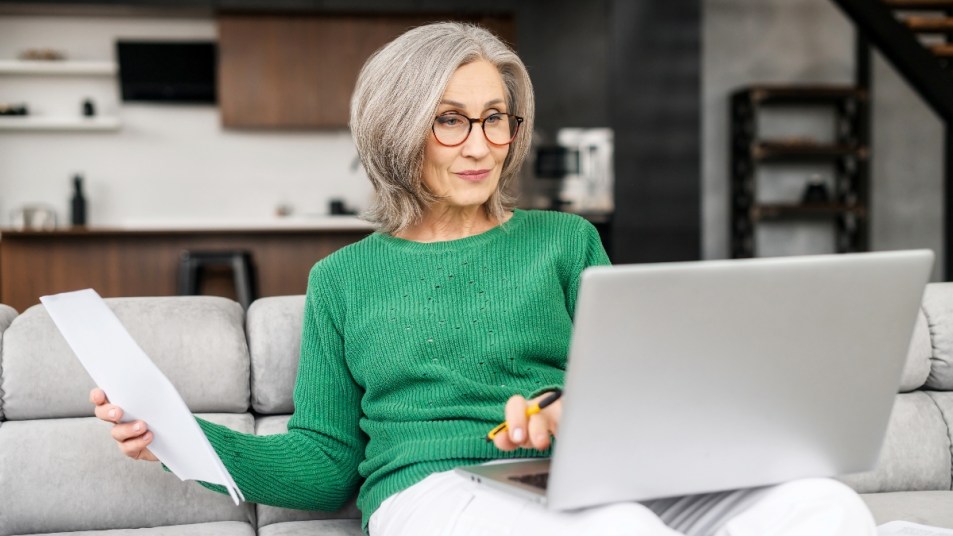 mature woman on laptop with papers in hand doing research on life insurance