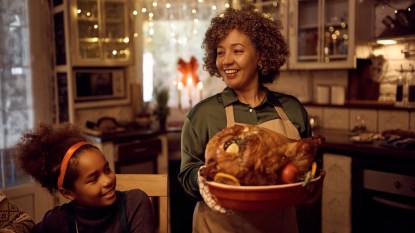Happy African American mature woman serving Thanksgiving turkey to her family in dining room.