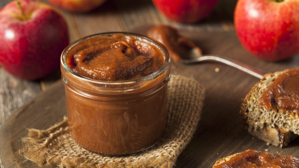 smooth apple butter in a glass jar next to toast and apples