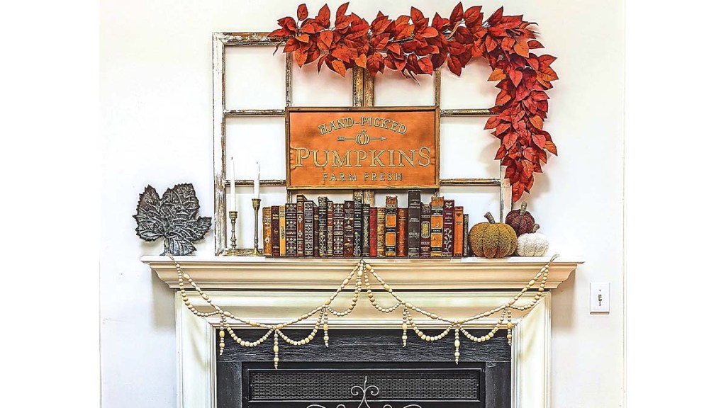 Fall mantel decor ideas: Cream fireplace mantel decorated in a chic vintage style with windowpanes, red leaf garland, vintage books, fabric pumpkins and candlesticks.