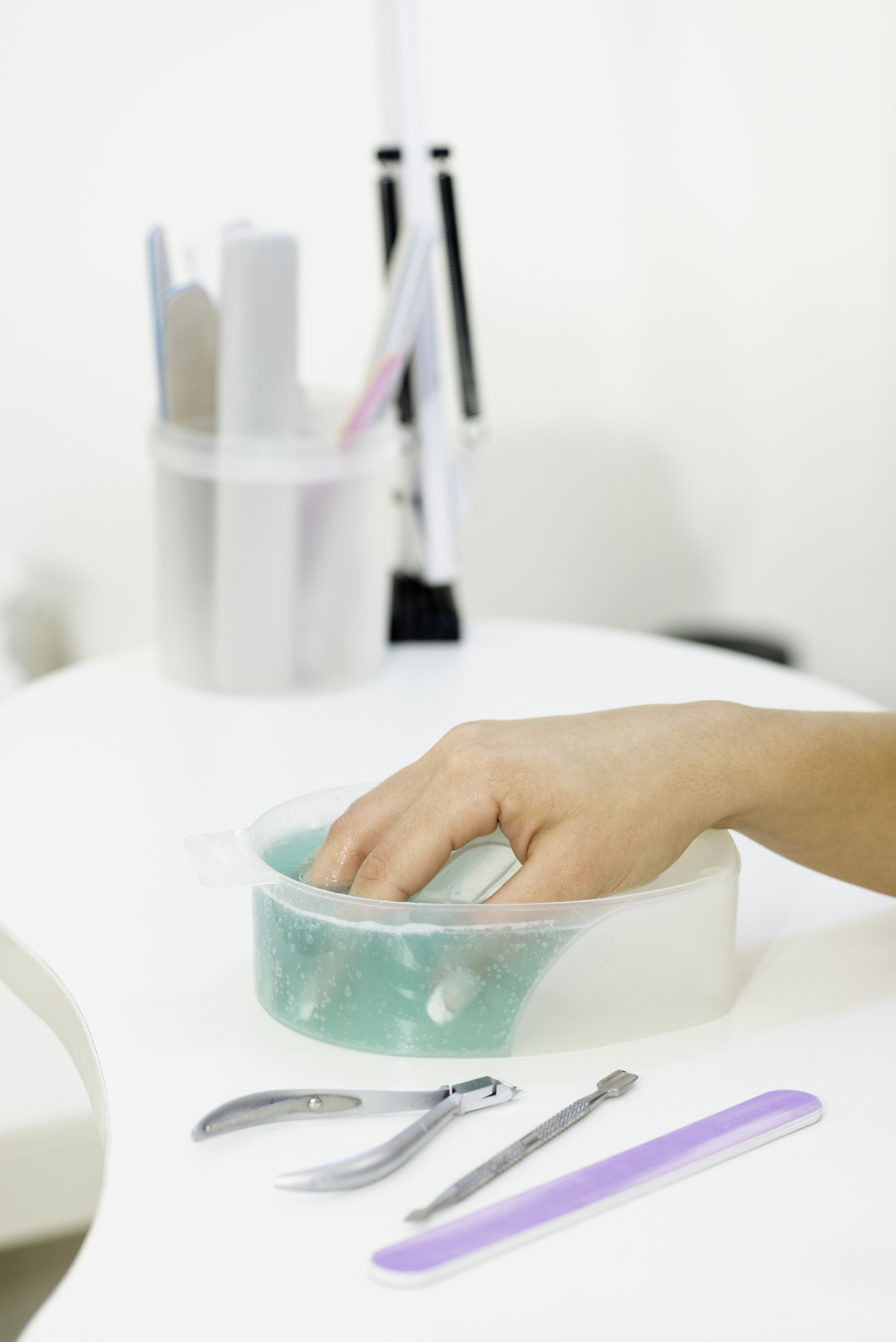 Woman soaking acrylic nails in acetone in plastic bowl.