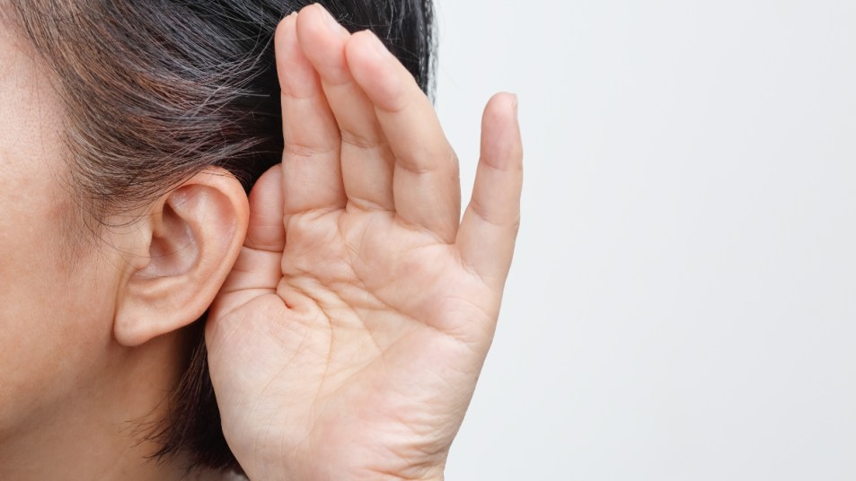 close up of mature woman with hearing loss from impacted earwax cupping her ear with her hand