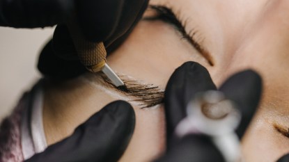 hands in black gloves performing microblading on woman