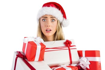 Woman in Santa hat holding pile of gifts and looking overwhelmed