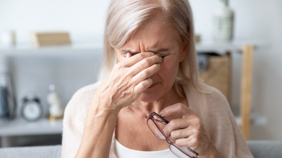 mature white woman suffering from a migraine, rubbing eyes with hand