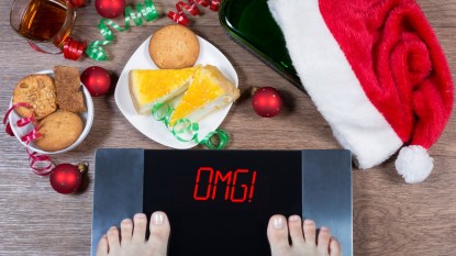 mature woman feet on scale with holiday foods around her, concept for holiday weight gain