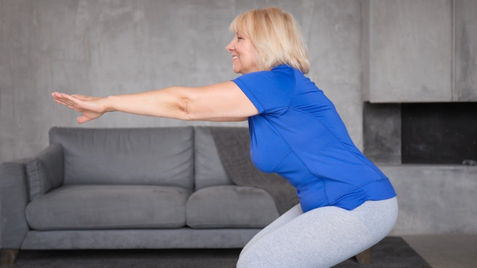 mature woman in blue shirt doing a squat as part of a leg workout