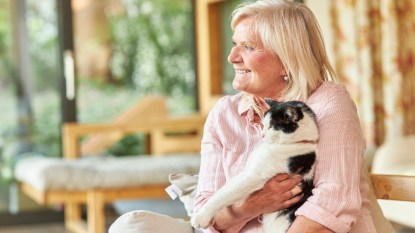 mature woman smiling and holding a senior black and white cat, her pet