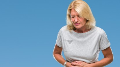 mature woman with blonde hair holding her stomach, concept for gut health and mental health