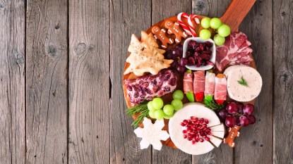 Christmas theme charcuterie board. Overhead view against a dark wood background. Mixed cheese and meat appetizers.