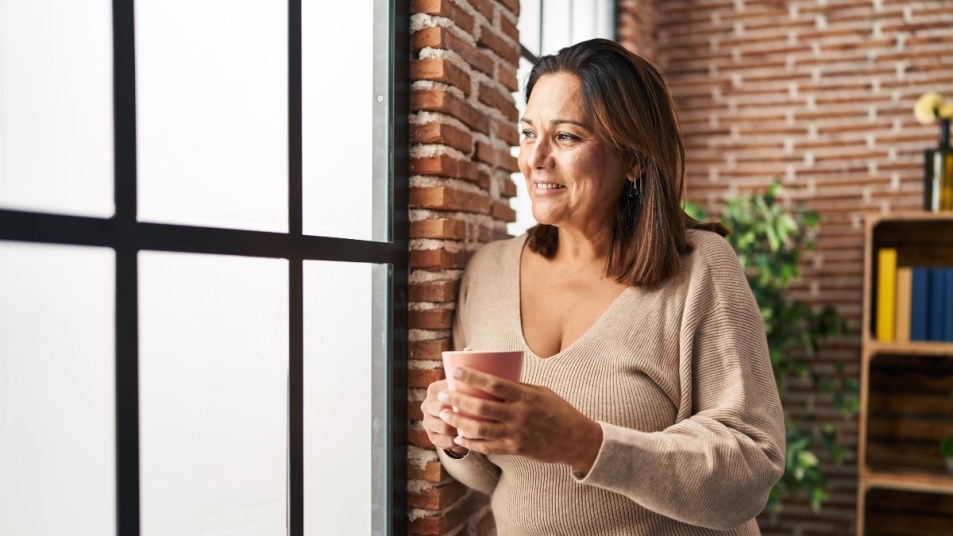 Middle age hispanic woman drinking coffee standing at home