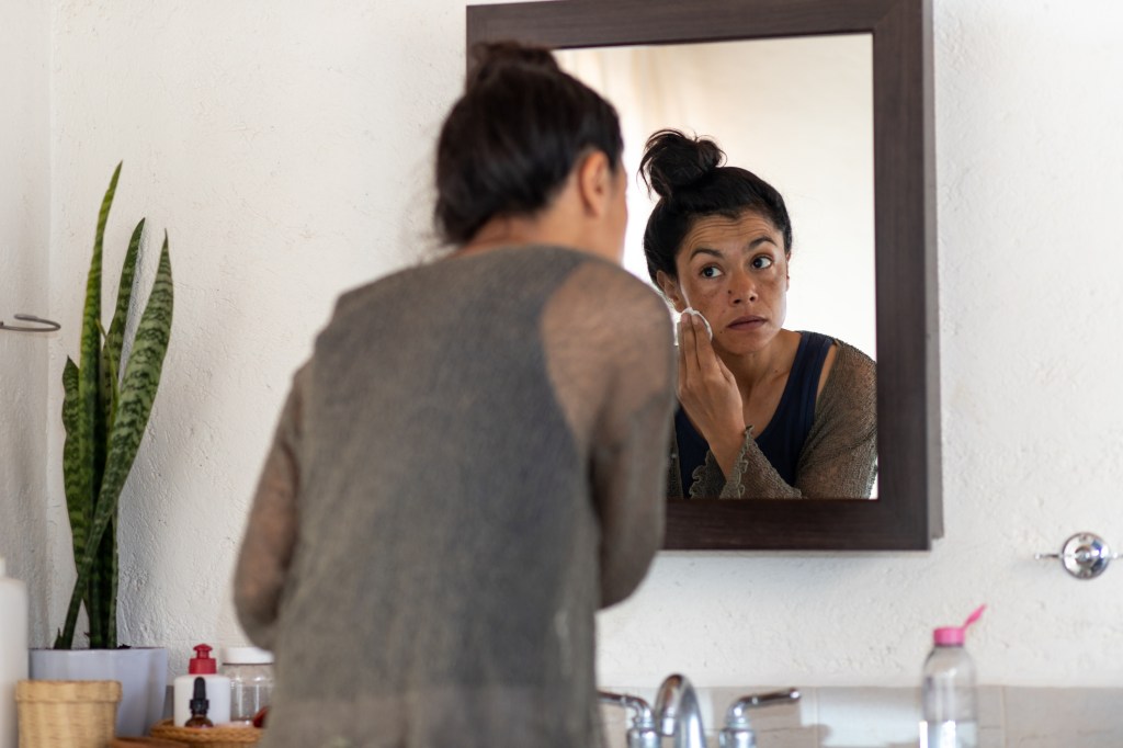 mature woman using micellar water to cleanse skin in mirror