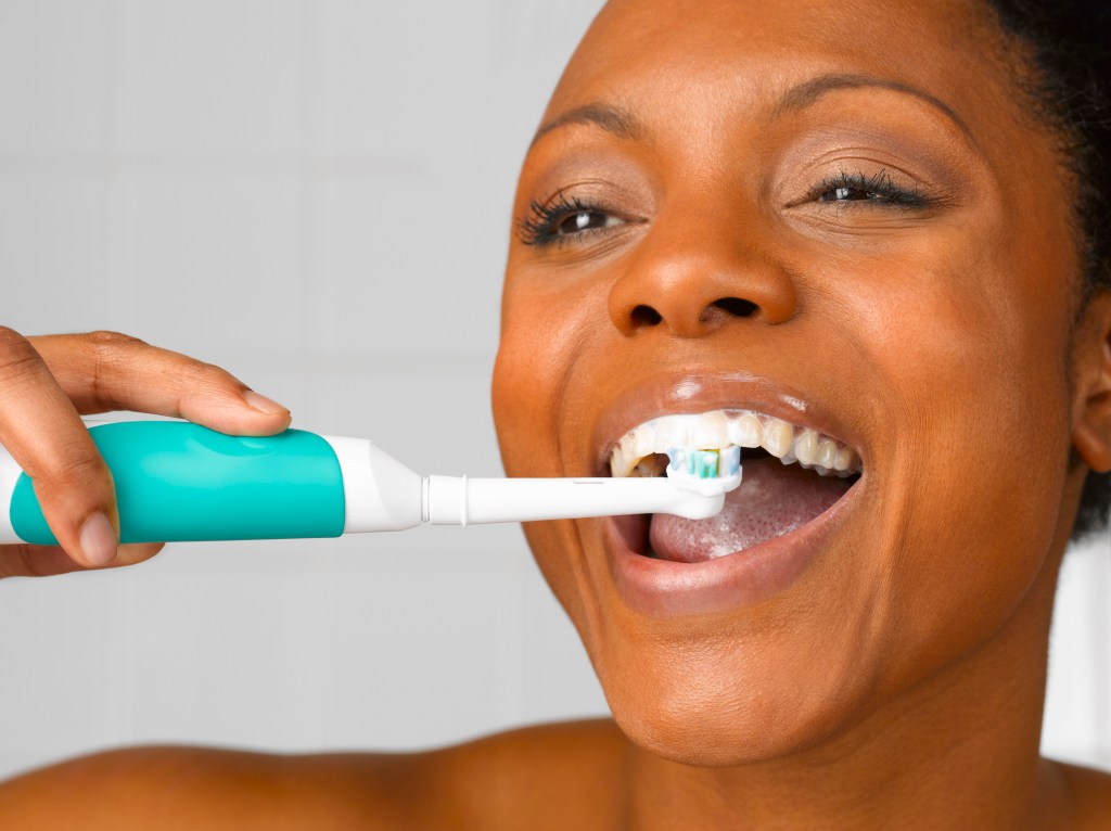 woman brushing teeth with electronic toothbrush