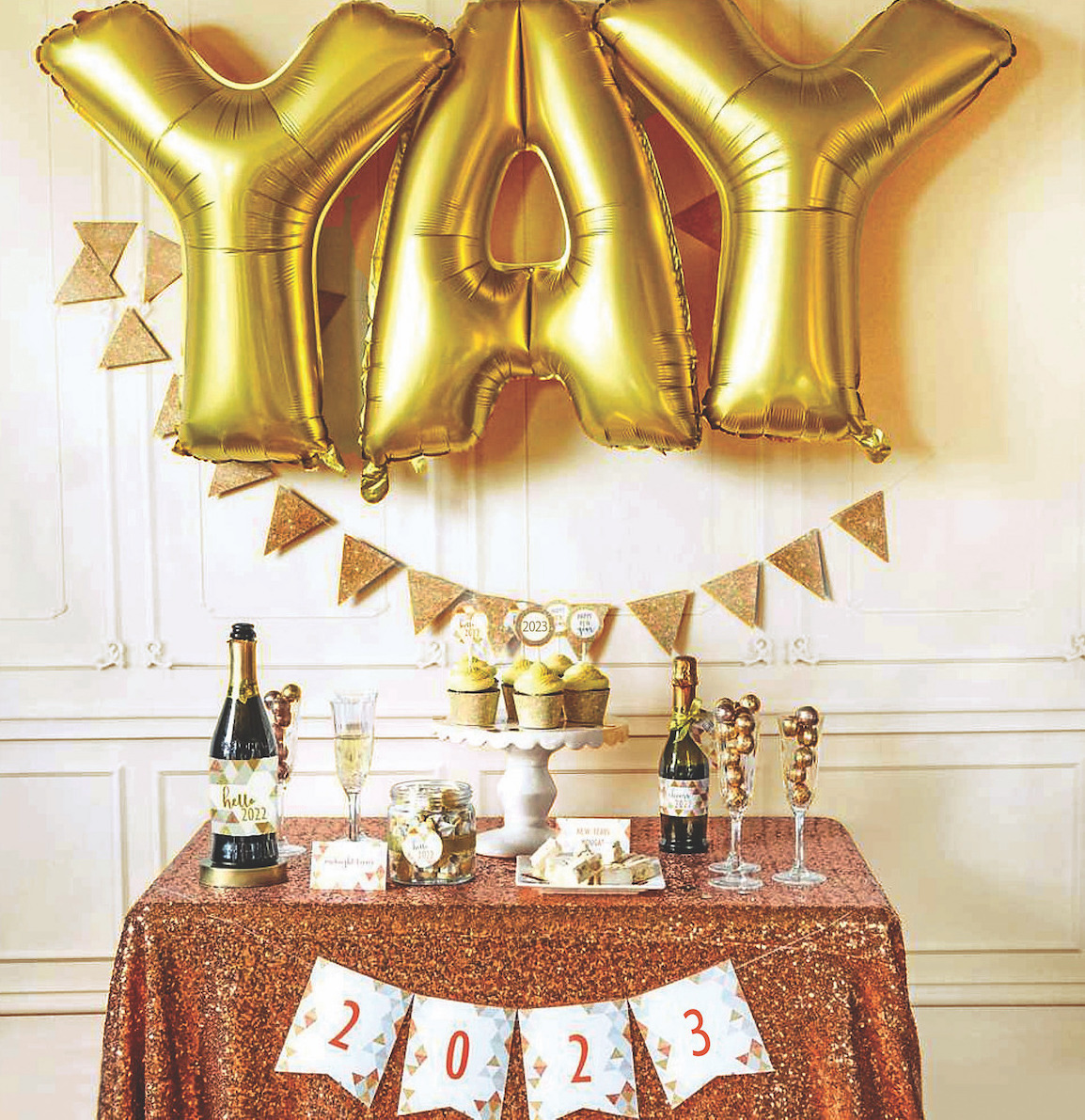 New Year's Eve party decorations with gold YAY balloons, champagne, cupcakes, and banners