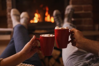A couple drinking hot cocoa together in front of a fireplace