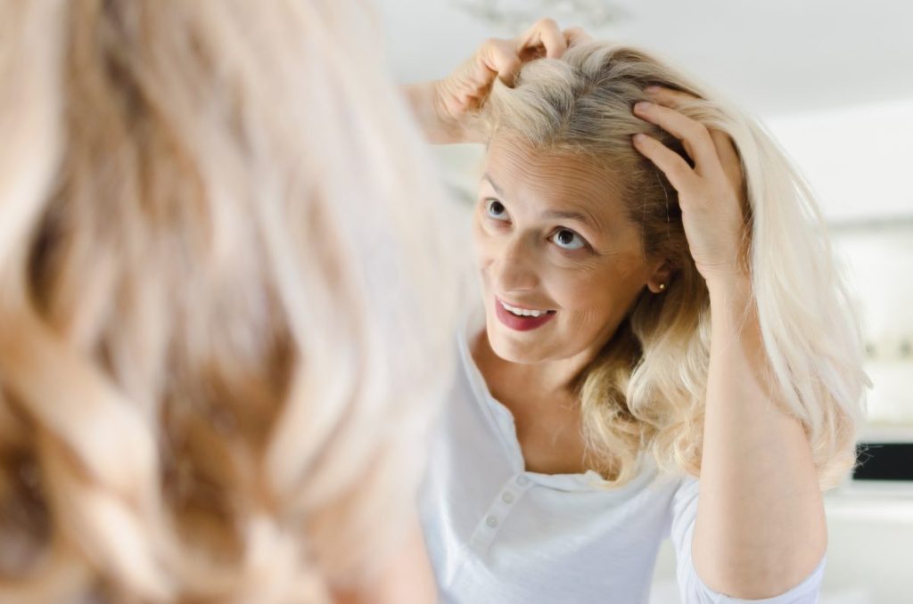 Beautiful happy senior woman checking her hair in front of a mirror at home.