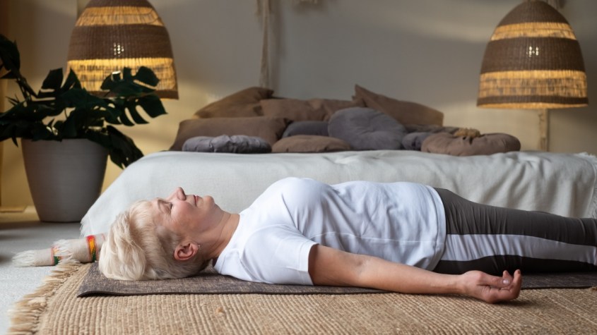 Senior caucasian woman lying on yoga mat after workout. Fit female relaxing on floor at home.