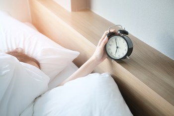 Woman hitting snooze button on alarm clock