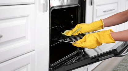 woman with yellow gloves cleaning an oven rack
