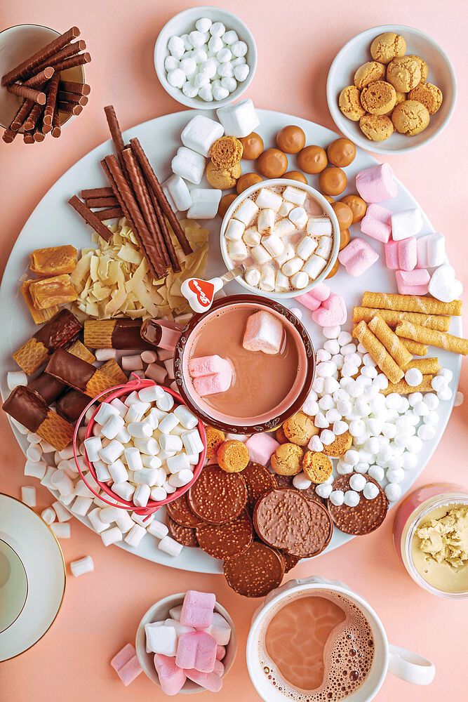 Hot chocolate, marshmallows, chocolates and cookies charcuterie board on pink background. Closeup view, horizontal orientation