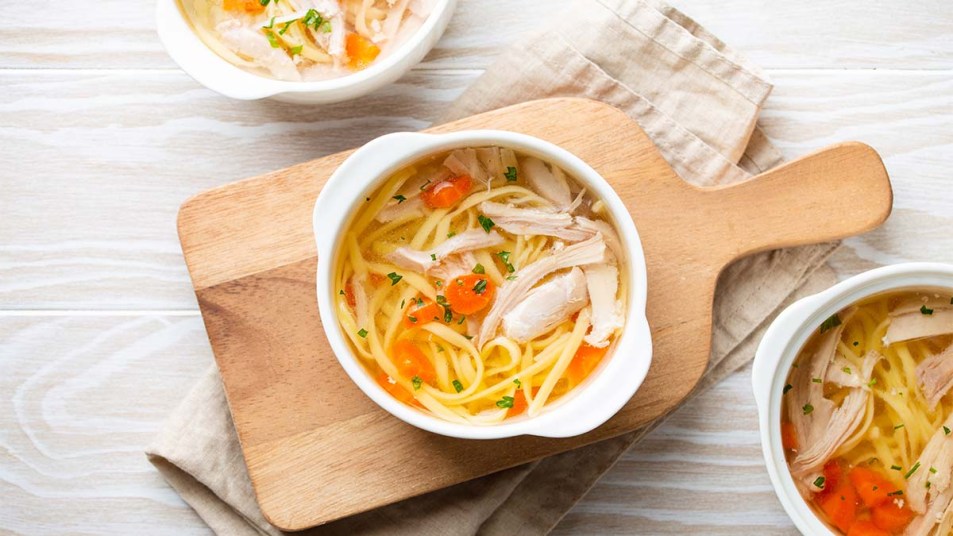 Warm healthy homemade chicken soup in white ceramic bowls on cutting board
