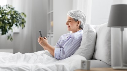mature woman in pajamas in bed on her phone, concept for bad winter habits