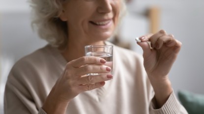 Woman smiling as she takes pill with glass of water