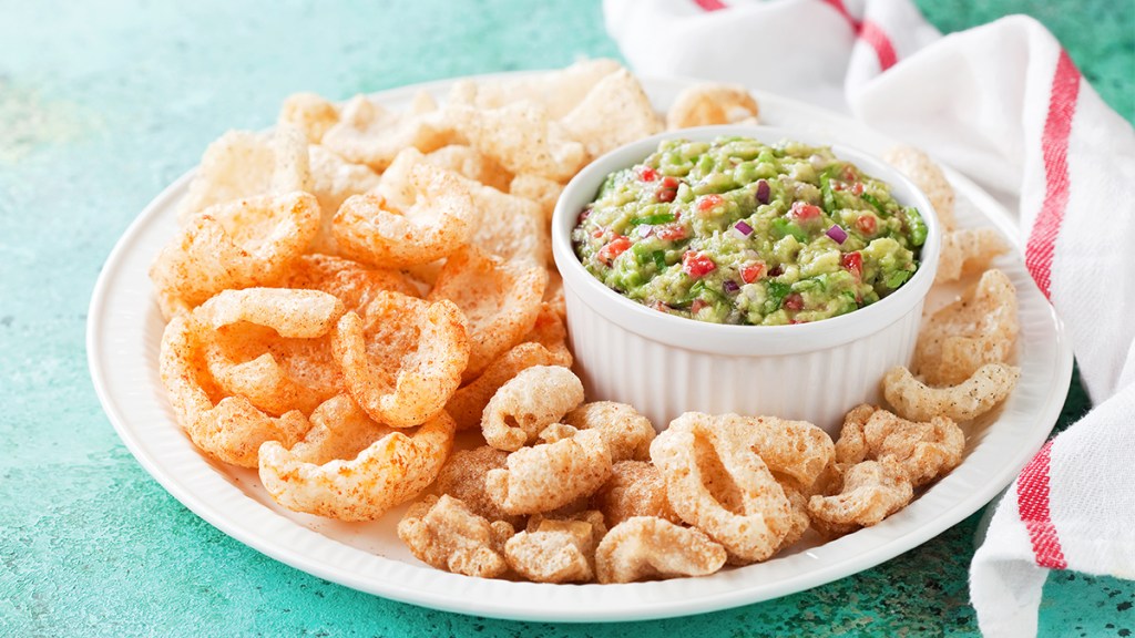 Bowl of guacamole made with collagen powder on a plate with pork rinds
