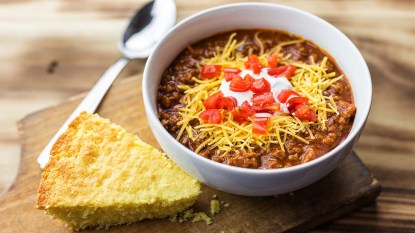 A bowl of chili with tomatoes, sour cream, cheese, and a piece of cornbread