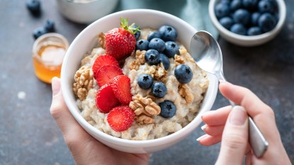 Hands holding a bowl of oatmea, which is rich in beta glucan,l topped with berries