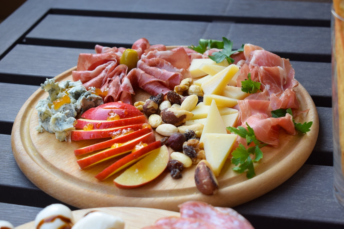 Charcuterie board with apple, meats, cheeses, and nuts and berries